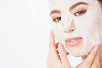 Beautiful young woman is getting facial clay mask at spa, lying with cucumbers on eyes