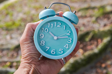 hand holding analog clock over nature background