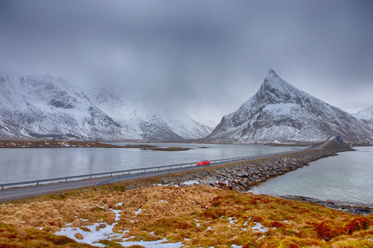 lofoten Islands In Norway. Red Noticable Car Passing by Fredvang Bridge At Lofoten Islands In Winter Time in Norway.