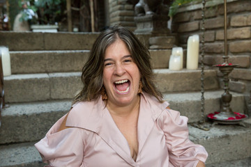 Woman laughing outside with a beige blouse on a stair background. Hysterical laughter concept. Hilarious and contagious laughter of a really good joke. Enjoying life. Girl having fun and feeling happy