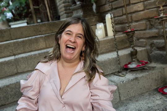 Woman laughing outside with a beige blouse on a stair background. Hysterical laughter concept. Hilarious and contagious laughter of a really good joke. Enjoying life. Girl having fun and feeling happy
