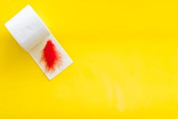 Toilet paper roll and feather for proctology diseases concept on yellow background top view mock up