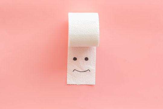 Toilet paper roll with painted face for proctology diseases concept on pink background top view