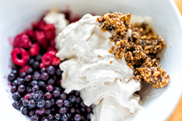 Macro closeup of bowl of vanilla ice cream topped with frozen blueberries bilberries granola and red raspberries berries