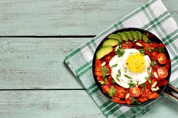  Chilaquiles mexican breakfast. tortilla chips are lightly stewed in a red tomato and paprika chili sauce, scrambled eggs are added and served in a pan with avocado and green onions and cilantro.