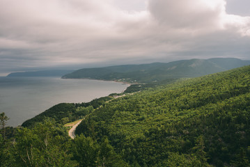 Fototapeta na wymiar A winding paved road through the evergreen forests on the coast the Cabot Trail in Cape Breton Nova Scotia just outside Cheticamp with clouds and sunlight visible