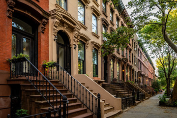 Scenic view of a classic Brooklyn brownstone block with a long facade and ornate stoop balustrades on a summer day in Clinton Hills, Brooklyn