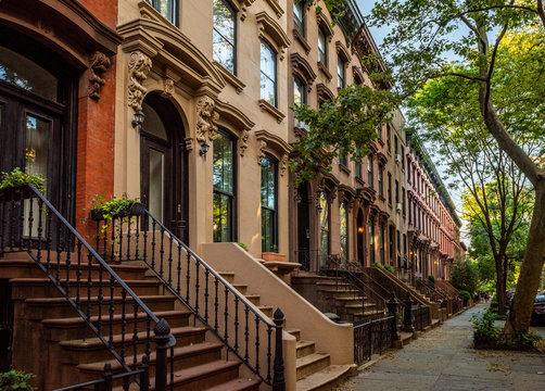 Scenic view of a classic Brooklyn brownstone block with a long facade and ornate stoop balustrades on a summer day in Clinton Hills, Brooklyn