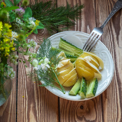 Young potatoes with cheese and slices of green cucumber in a white plate
