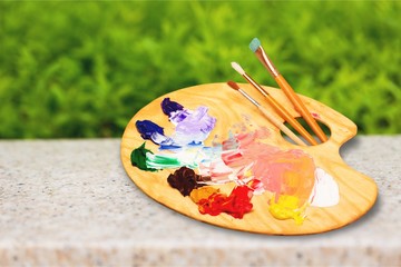 Wooden art palette with blobs of paint and a brushes