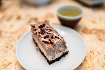 Macro closeup of chocolate coconut tiramisu vanilla cheesecake bar dessert raw vegan dessert on white plate with cacao nibs topping and green tea