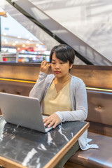 Short hair Asian woman working on laptop on coffee table
