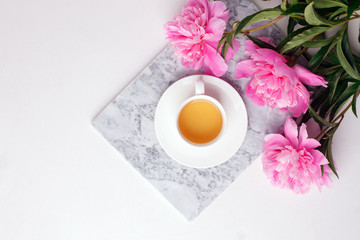 Obraz na płótnie Canvas Fashion blogger styled desk frame with flowers, cup of herbal tea, pink peonies on marble plate on white, breakfast morning lifestyle, minimal concept, copy space