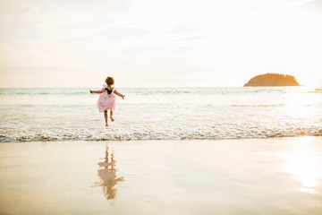 Fototapeta na wymiar Cute little girl jumping on the beach. Sunset time. Kid having fun in holiday vacation with back sun light - Youth, lifestyle, travel and happiness concept