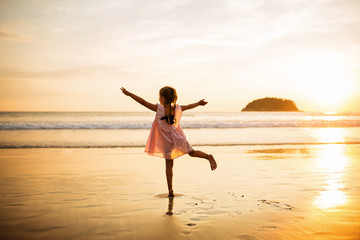 Cute little girl walking on the beach. Sunset time. Kid having fun in holiday vacation with back sun light - Youth, lifestyle, travel and happiness concept