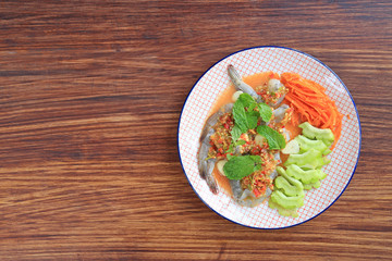 Delicious raw Shrimp in seafood chilli sauce with mint leaf and vegetables in plate on wooden table background.