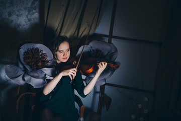 a beautiful girl plays the violin among the big artificial flowers in the twilight. Babe in dress...