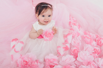 a little girl in a pink dress sits on the floor on background of flowers. Child promotes children's clothes