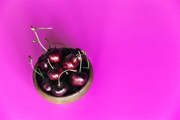 Fresh cherries in a small bowl on a bright pink background with copy space on the right