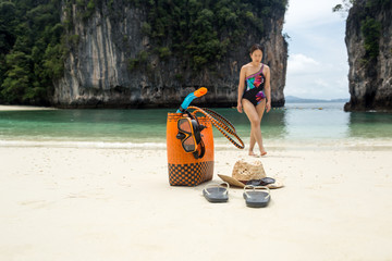 Beach bag and travel accessories with woman in blur background on vacation.