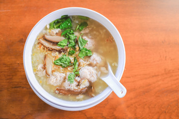 A bowl of rice porridge with minced pork, mushroom,  clear soup for breakfast, serving on wooden table
