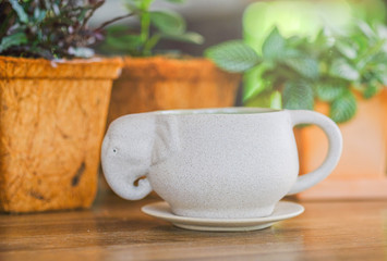 a coffe mug designed elephent shape and sourcer on wooden table and green plant background and brown baseket for creative idea 