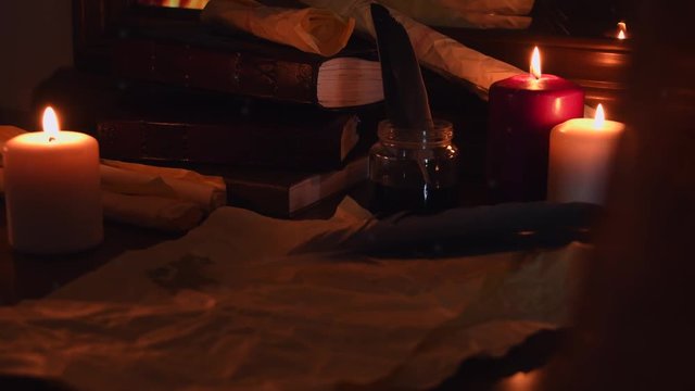 Detail of an old scribe room next to a fireplace with vintage paper, books, feathers, candles and a curtain moving in the wind and dust flying around