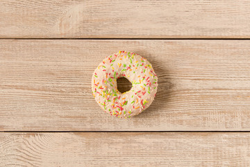 Fresh glazed donut with colorful sprinkles on a wooden table.