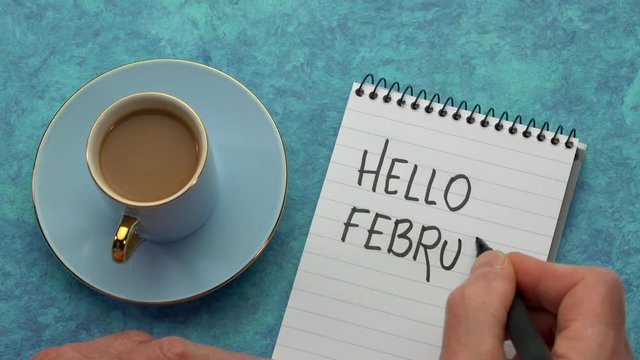 Hello Febuary - a man hand writing a note with a black marker in a notebook, overhead view with a cup of coffee