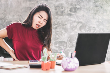 Asian woman suffering from lower back pain sitting too long on chair working on computer, office syndrome concept background