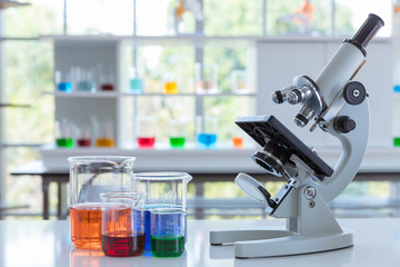 The scientific microscope with the scientific glassware on the white table.