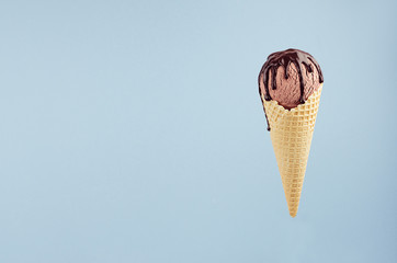 Brown ice cream in crisp waffle cone with chocolate sauce on pastel blue background, mock up for design.