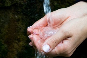 water flows into women's hands, hands with splashes of water, pure spring water