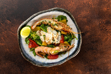 Plate of fresh salad with shrimps and tomatoes at concrete background.
