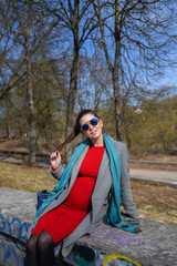 Pregnant girl in a red dress in the park. Portrait of a beautiful pregnant woman in a red dress and blue scarf, in a gray coat.