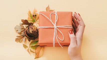 Autumn birthday present. Woman hand holding handmade red paper gift box. Fall leaves and chestnut...