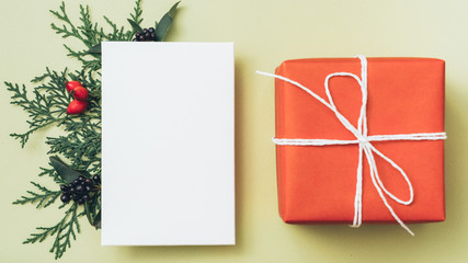 Holiday greeting set. White mockup paper, orange gift box with green juniper decor and fall berries on olive background.