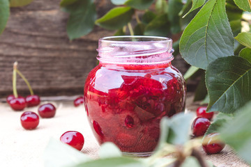 Fresh cherry jelly with fruit on a wooden background near the berries and green leaves.