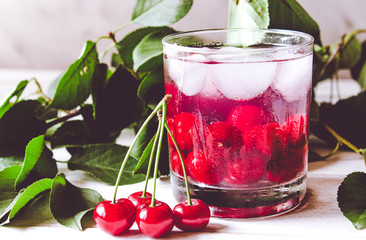Fresh cherry cocktail with ice on a white wooden background. Fresh summer cocktail with cherries and ice cubes.