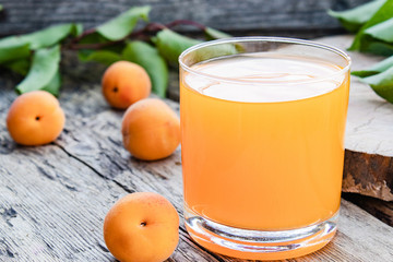 Fresh apricot juice with apricots and a branch with green leaves on the background of old boards.