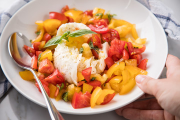 Frau isst Mozzarella Kugel mit roten und gelben Tomaten, Basilikum und Olivenöl auf Teller und  Marmor Hintergrund