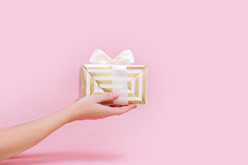 Womans hands holding gift or present box on pink pastel background.