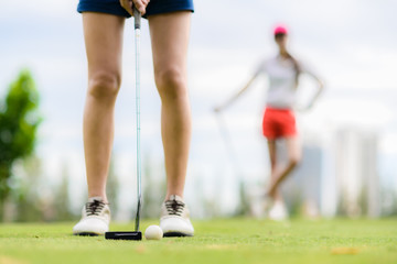 Obraz premium golf ball being putt by woman golf player on the green at golf course, opponent competitor waiting to putt in background