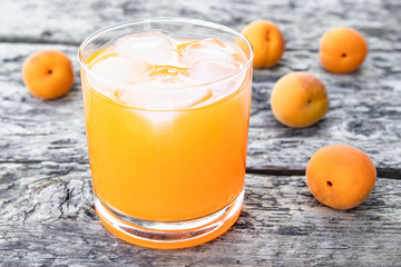 Fresh apricot juice with apricots and ice cubes in a glass against the background of old boards. Summer soft drinks.