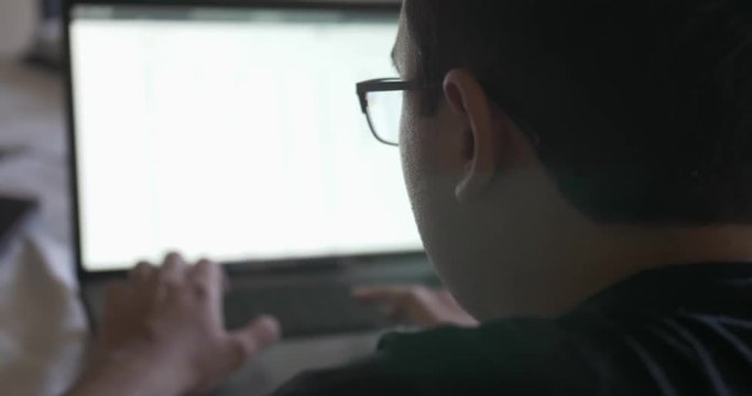 Close up shot from the back of man with glasses working with a laptop, using the keyboard and trackpad.