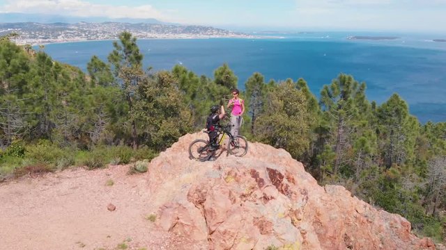 Aerial over couple of people slapping hands at top of Esterel mountain by the sea.