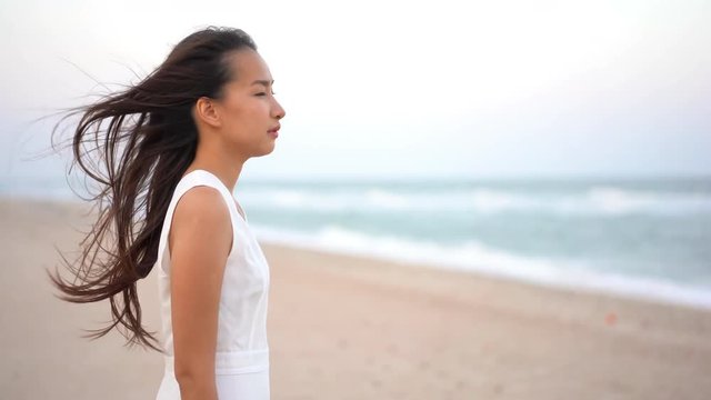 Asian woman at the beach on a windy day with a worried look on her face and wind in her hair, day, static camera, eye level shot, real time