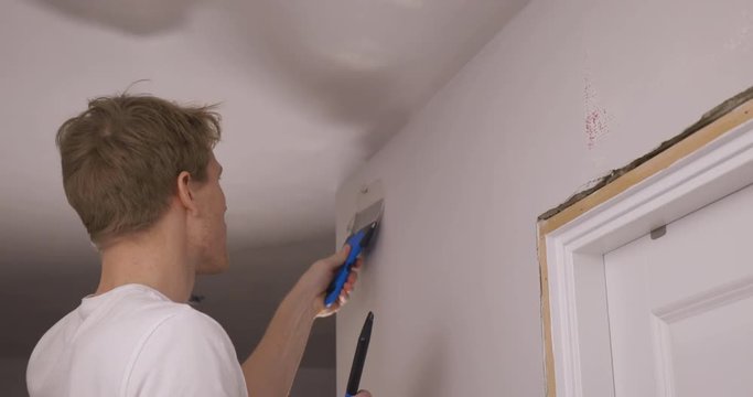 Man repairs wall by putting on spackle with a spatula. Refurbishment project.