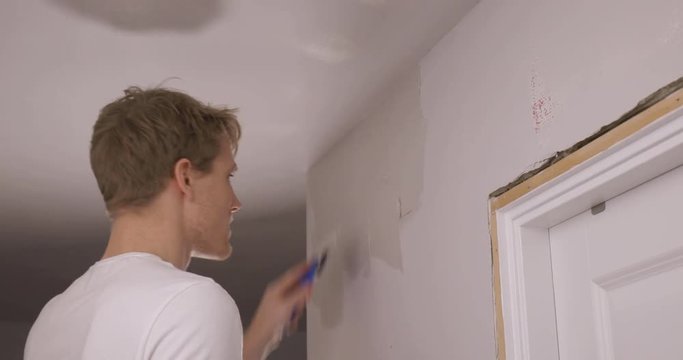 Man repairs wall by putting on spackle with a spatula. Refurbishment project.