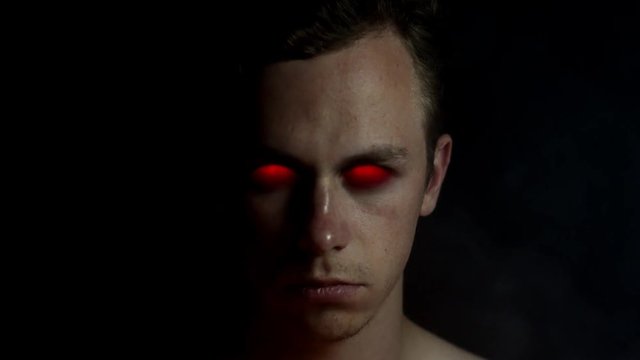 Evil underworld demon devil spirit from hell with red glowing eyes and smoke around him looking into camera.